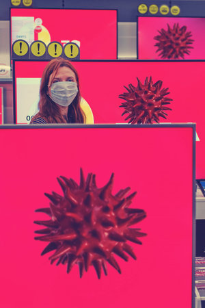 Redhead woman in a medical mask on the background of televisions with the image of a coronavirus on...