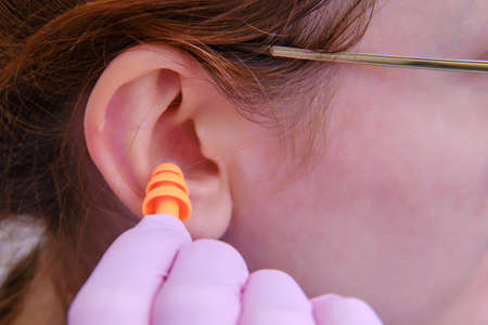 A woman inserts earplugs into her ear in protective medical gloves, close-upの写真素材