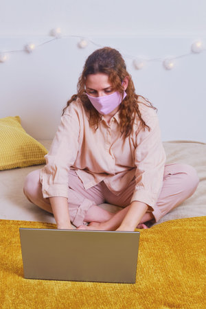 Problems of remote work online during quarantine isolation. A woman in a medical mask works at a...