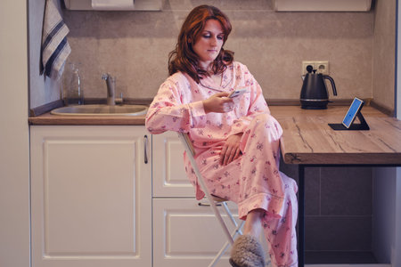 Young woman with a tablet and phone in her own kitchen. Work from home during quarantine and...