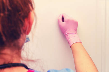 A doctor in protective medical gloves knocks on the apartment doorの写真素材