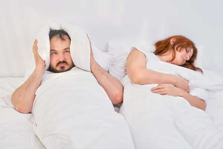 The man covered his head with a pillow due to his wife's snoring. Trouble sleeping in the family. Relationship problems coupled with isolation due to coronavirus.の写真素材