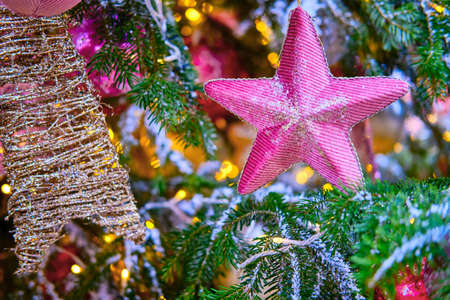Pink soft star hanging as decoration on a snow covered Christmas tree, close-upの写真素材