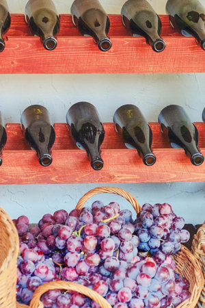 Homemade wine from natural grapes. Basket with red and white grapes. Bottles of wine on the shelves.