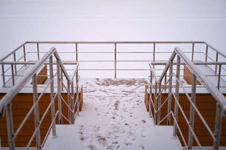Stairs with handrails for descending to a winter snow-covered pondの写真素材