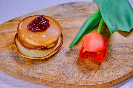 Red Tulip next to a stack of pancakes. Hot homemade cakes on a wooden table. Berry jam on top of pancakes and purple flowers.の写真素材