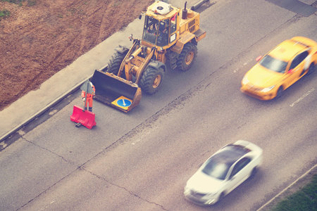 A worker prepares to carry out repair work on the road by removing signs from the bucket of an...