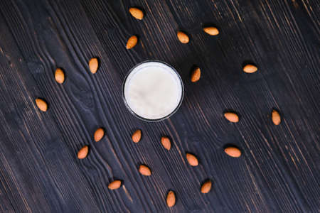 Nuts scattered on a table, top view. Almond milk on a black wood background. Cup of milk and almonds on a dark wooden background.の写真素材