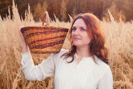 A woman with a basket and a musical instrument flute stands in a fieldの写真素材