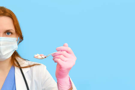 A doctor in a white uniform with a spoonful of pills in his hand on a blue background, copy space.の写真素材