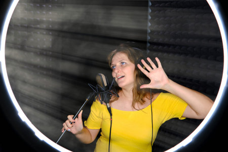 Young woman sings in a recording studio on black background. Professional microphone black colors,...