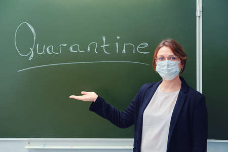Woman teacher stands next to the inscription Quarantine on the school blackboard. Teaching students via the Internet in quarantine during the coronavirus pandemicの写真素材
