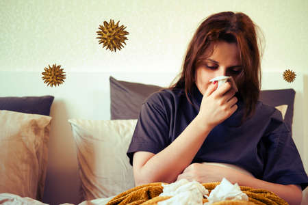 A woman with the coronavirus virus in bed in quarantine. Collage of a woman in isolation at home with virus moleculesの写真素材