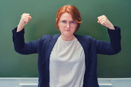 Teacher raised her hands showing muscles on the background of the school boardの写真素材