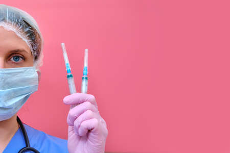 Woman doctor with insulin syringes in hand on a red background, copy space for text. A nurse in a medical mask is preparing for an injection, conceptの写真素材
