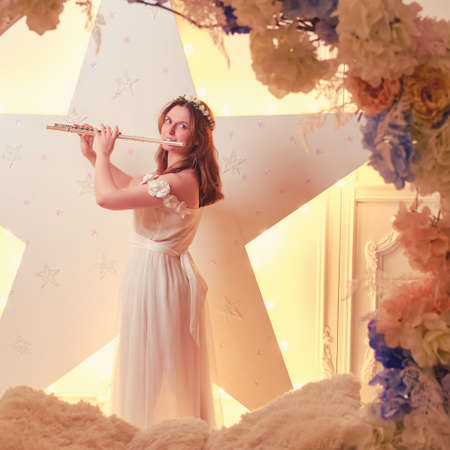 A female musician plays a flute in a ring of flowersの写真素材
