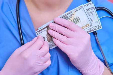Us dollar bills in the hands of a doctor during quarantine. Concept of remuneration for medical workers and doctors in America during the coronavirus epidemic.の写真素材