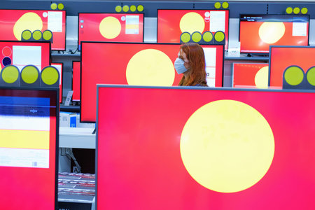 Redhead woman in a medical mask on a background of televisions, copy space