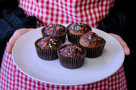 Woman with cakes in a candy coating. Plate with chocolate muffins on the background of a girl in an apron.の写真素材