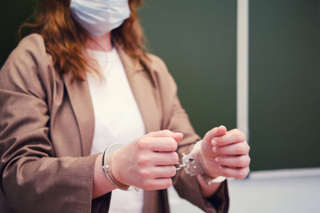 Woman teacher in handcuffs stands at the blackboard, concept of problems with coronavirus. The...
