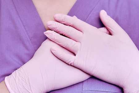 Concept of stay at home, hands folded over the heart. Doctor in protective gloves and medical uniform, close-up.の写真素材