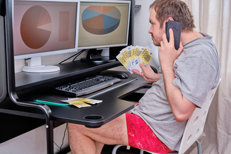 A man in male red shorts is sitting with euro money in his hand. Work from home during isolation due...