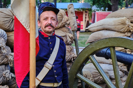 Moscow \ Russia 06 07 2019: Gunner with the flag of the French army in clothes of the 19th century. A soldier of the Russian-French war stands next to a gun in military uniform.のeditorial素材