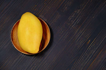 Ripe mango on black wooden background. Tropical fruit on a wooden plate, close-up. Big yellow mango with copy space for text.の写真素材