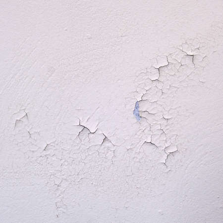 Spoiled fresh white paint close-up. Cracked new paint on a white wallの写真素材