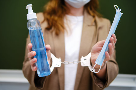 School teacher chained with handcuffs stands with sanitizer and medical mask, virus problem concept