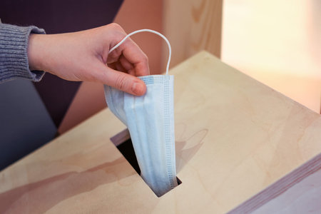 A hand puts a donation of a medical mask in a wooden box. Concept of helping people during the...