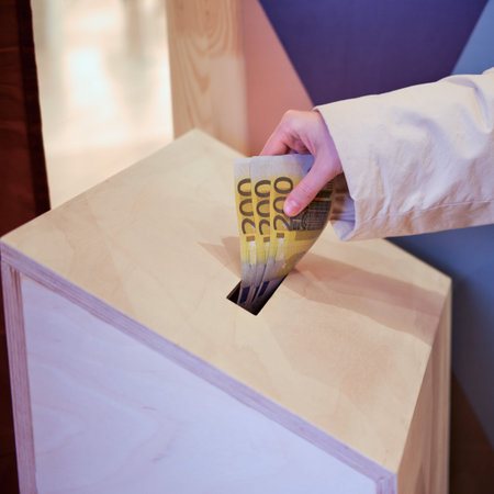 A hand puts donations in money euros in a wooden box. Assistance to those in need during the...