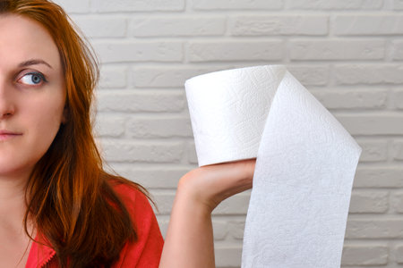 Portrait of a woman with a white roll of toilet paper in hand, brick wall backgroundの写真素材