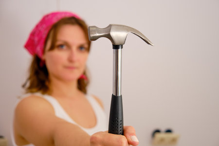 Woman holds hammer on outstretched arm in front of herself, copy spaceの写真素材