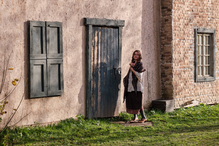 A brunette woman stands with flowers at the old wooden door. European house with architecture in the...