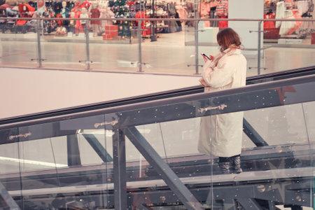 People with face masks ride an escalator to a shopping mall with storeの写真素材
