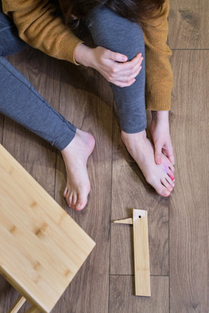 Woman fell from a wooden ladder at home and holds on to her injured leg. Stepladder made of wood broke under a man while working at homeの写真素材