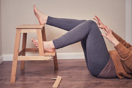 The woman fell from a wooden stepladder and suffered a leg injury. Problems with safety at work at homeの写真素材