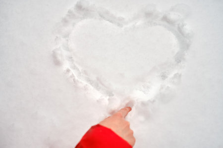 Woman hand draws a heart in the snow, copy space for text. Girl painting a heart on a snowy winter surface on valentine dayの写真素材