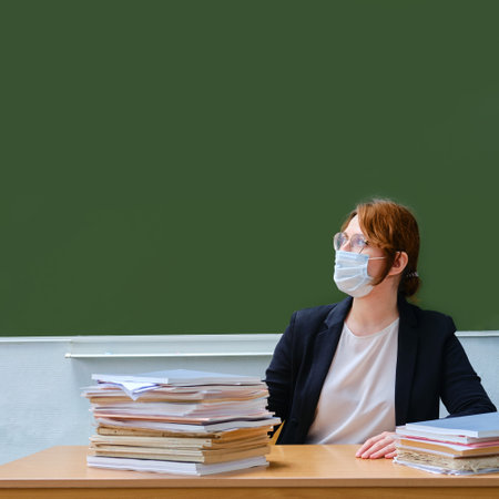 A woman is sitting at the teacher desk in a medical mask, copy space. The concept of training and conducting classes during the coronavirus epidemicの写真素材