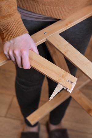 Young woman showing broken leg of wooden chair. Problems with labor protection when working at homeの写真素材