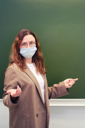 School teacher in a medical mask stands at the blackboard and points at you. School quarantine education conceptの写真素材