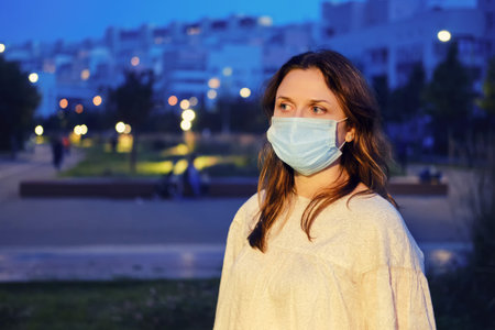 Night portrait of a woman in a medical mask on the background of the parkの写真素材