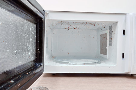 A dirty microwave oven with an open door in need of washing and cleaning. Hygiene problems and cleaning of kitchen appliancesの写真素材