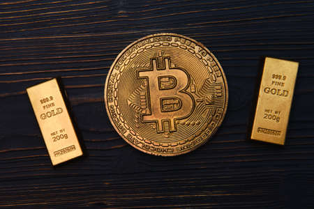 A bitcoin coin and gold bars lie on a wooden surface, black backgroundの写真素材