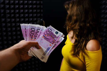The woman turns away from the money on a black background. Refusal to receive money in the recording Studio. Payment for recording a song at the concert of the singer.の写真素材