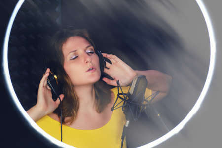 A young woman in a ring of light at a recording studio, copy space. Singer in yellow clothes on a black background near the microphone, copy space ..の写真素材