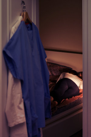 Female doctor sleeps at home in bed after a difficult shift at work, uniform hanging on the door of the roomの写真素材