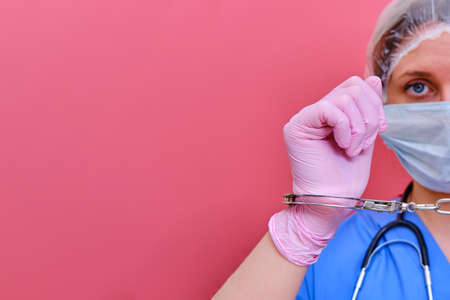 A woman medic holds a us dollar bill cut in half, copy space for text. A woman nurse with money for work on a pink background, the concept of paying doctors in a crisis due to the coronavirus epidemic.の写真素材