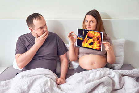 A pregnant woman shows a man an ultrasound with an unborn child. The husband looks incredulously at...